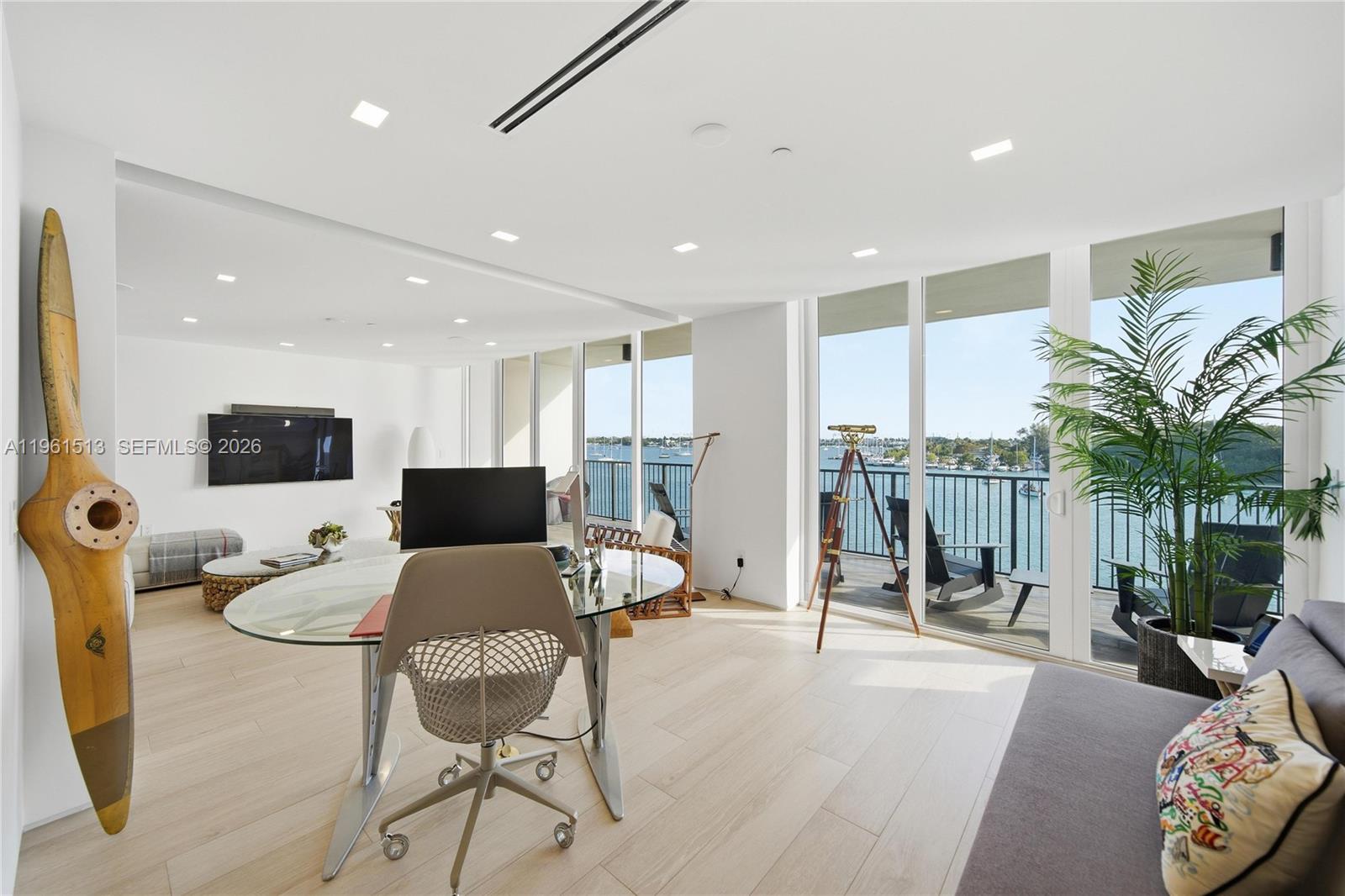 A modern living room features a glass desk, a vintage propeller, and a balcony overlooking water — 1000 Venetian Way # 403, Miami Beach FL 33139, MIAMI BEACH, FL