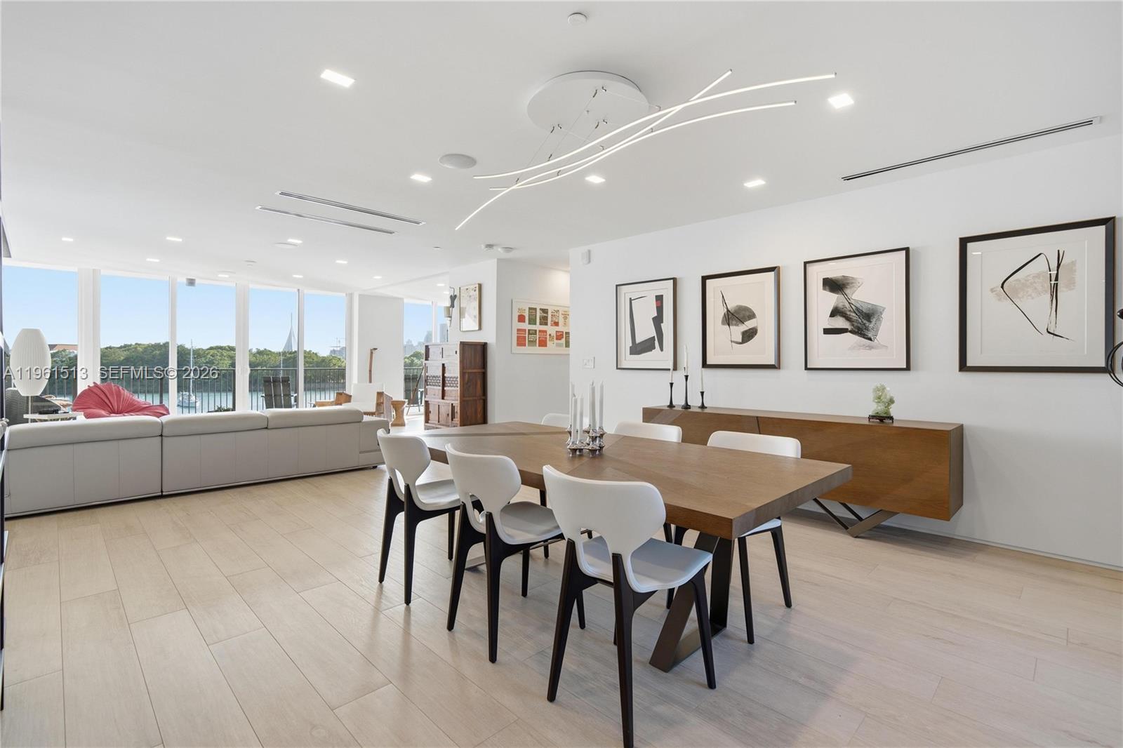 A modern dining area features a wooden table, white chairs, and large windows overlooking water — 1000 Venetian Way # 403, Miami Beach FL 33139, MIAMI BEACH, FL