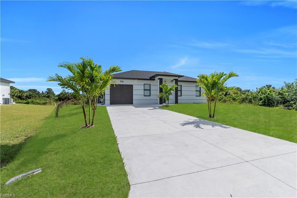 A single-story house with a concrete driveway, a garage, and palm trees in the yard — 713 ROMA AVENUE S, LEHIGH ACRES, FL