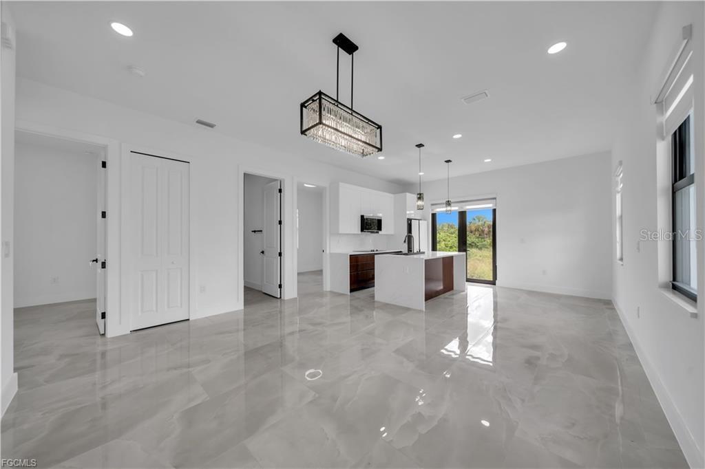 A modern open-concept kitchen and living area features white cabinetry, a central island, and tile flooring — 713 ROMA AVENUE S, LEHIGH ACRES, FL