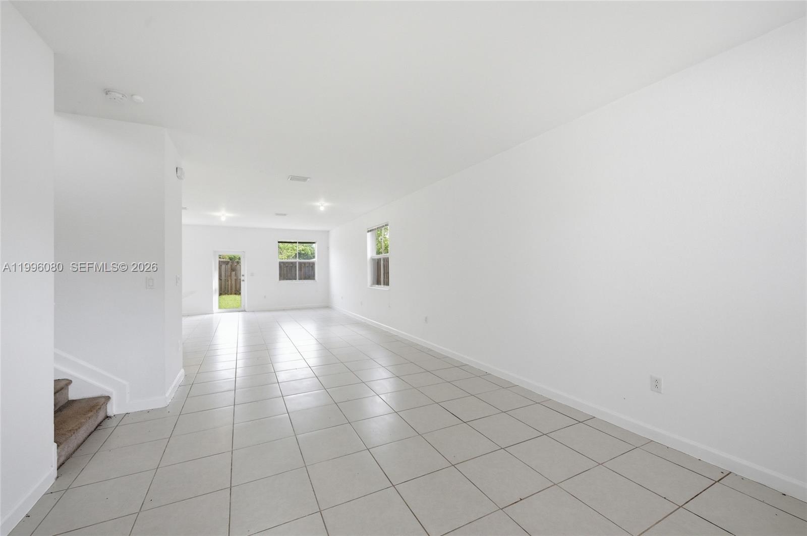 An empty living room features white walls, light-colored tile flooring, and a staircase — 2345 NW 131st Cir # 2345, Miami FL 33167, MIAMI, FL