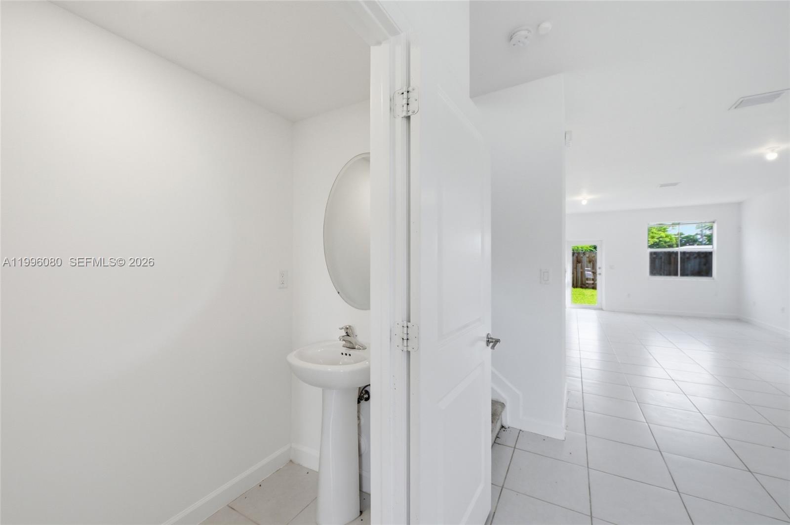 A small powder room with a pedestal sink sits beside an open-concept living area — 2345 NW 131st Cir # 2345, Miami FL 33167, MIAMI, FL