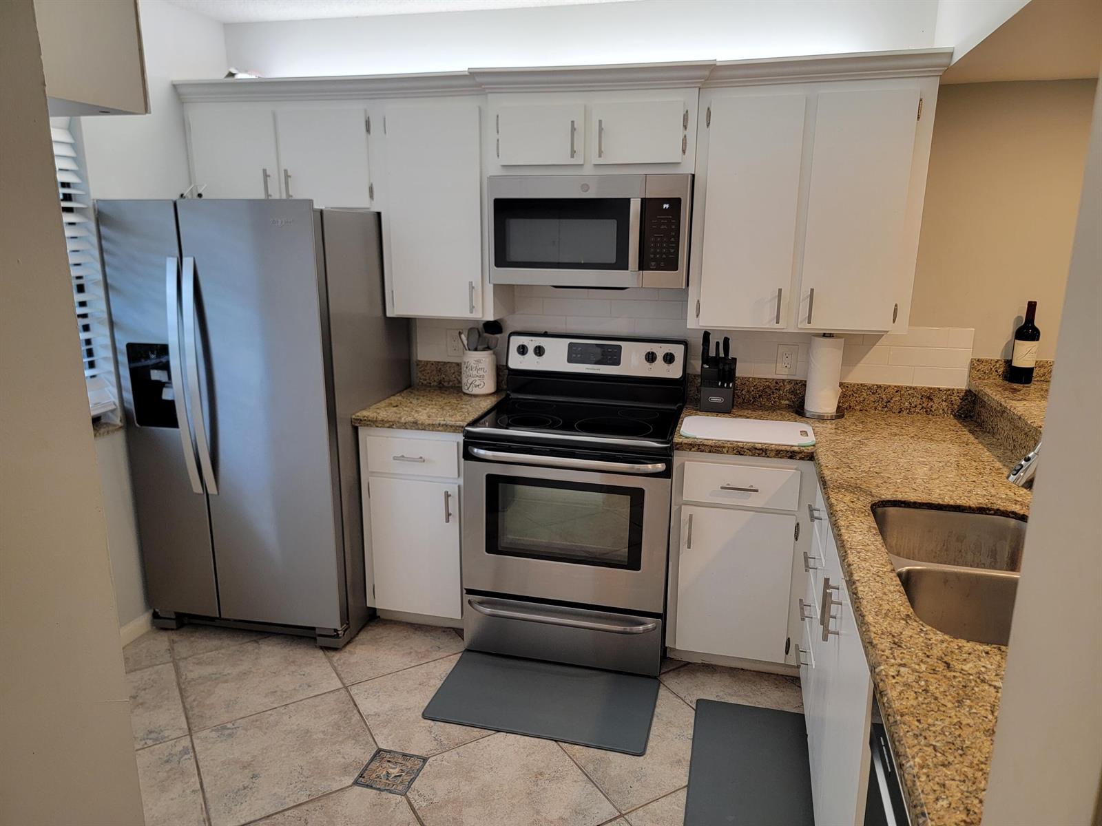 A kitchen features white cabinets, granite countertops, stainless steel appliances, and tiled flooring — 3540 Whitehall Drive # 106, West Palm Beach FL 33401, WEST PALM BEACH, FL