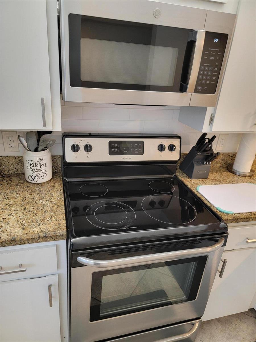 A kitchen features a stainless steel microwave above a black electric range and granite countertops — 3540 Whitehall Drive # 106, West Palm Beach FL 33401, WEST PALM BEACH, FL
