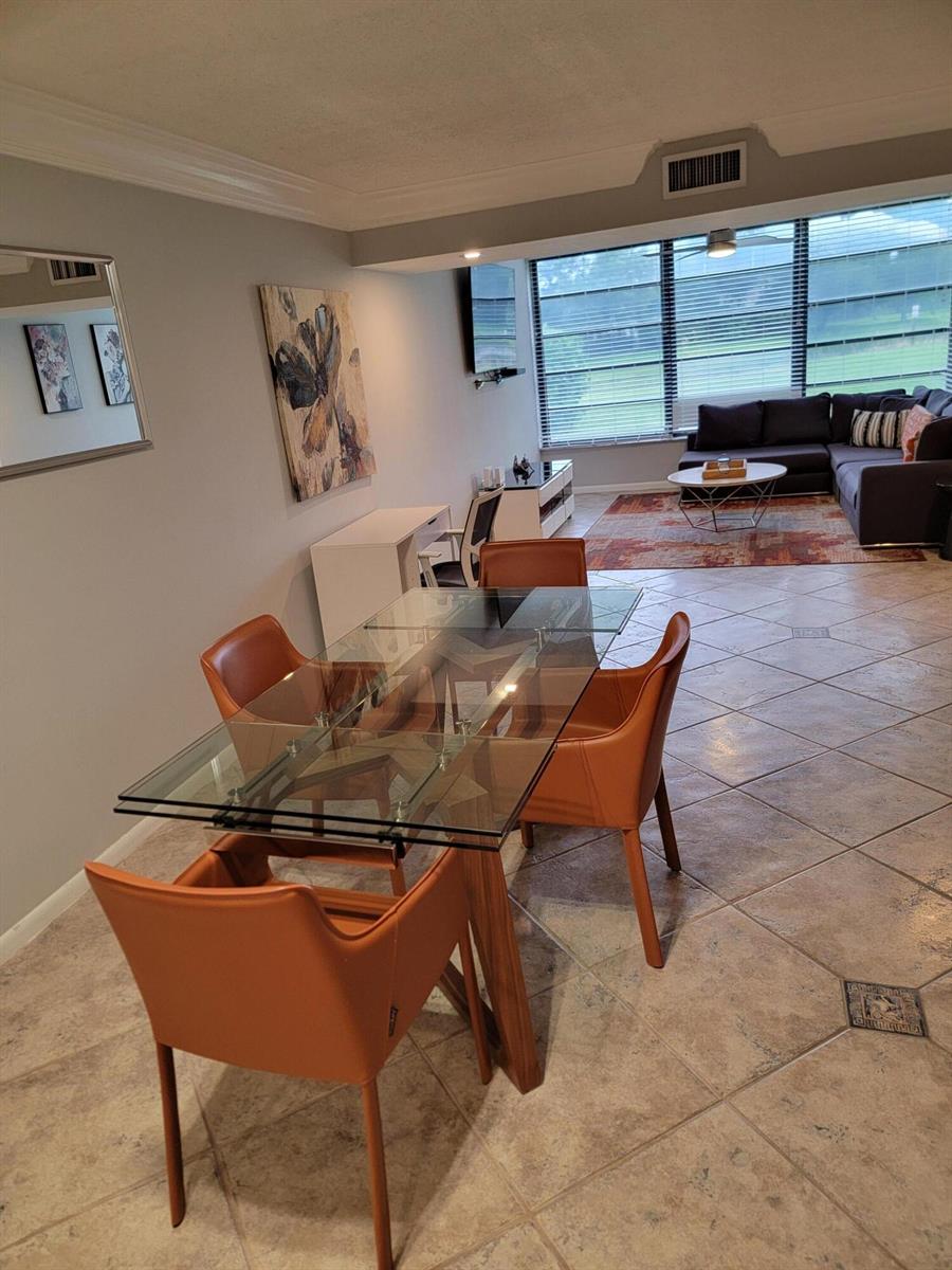 A dining area with a glass table and orange chairs opens into a living room — 3540 Whitehall Drive # 106, West Palm Beach FL 33401, WEST PALM BEACH, FL