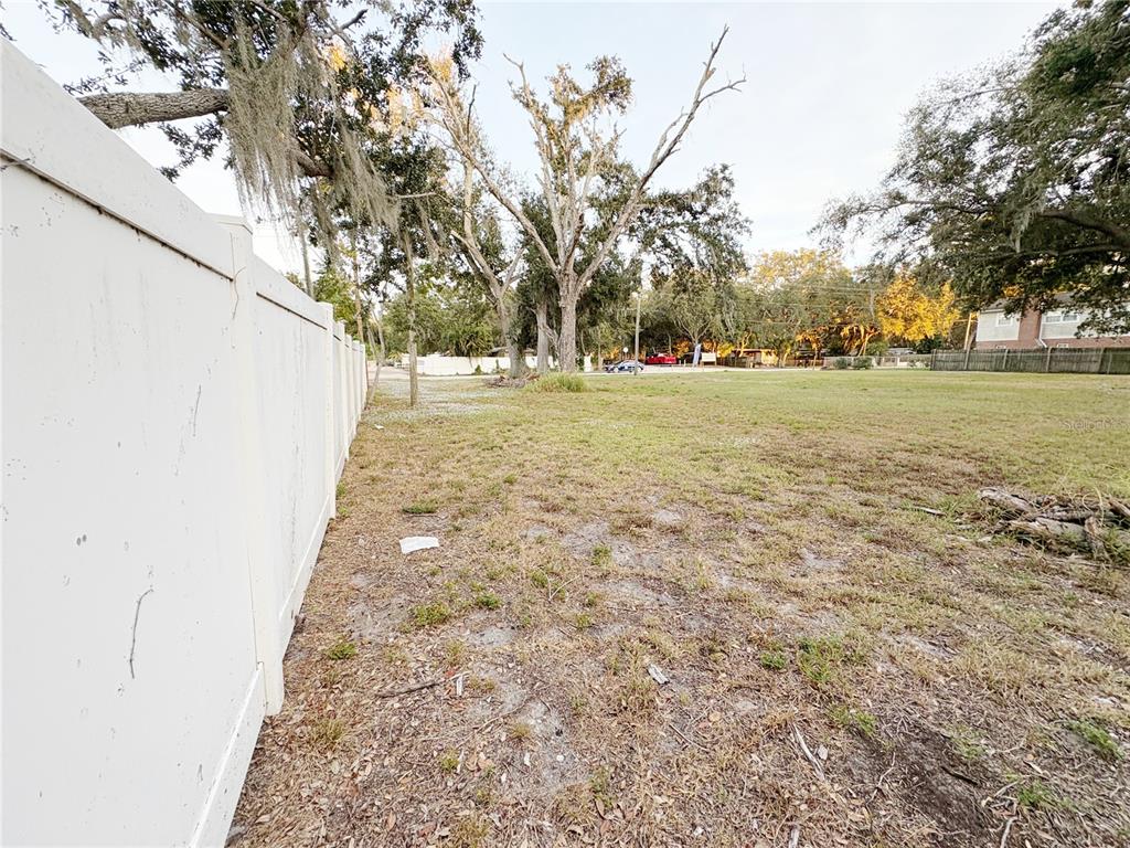 A white vinyl fence runs along the side of a grassy, partially wooded vacant lot — 6227 KRYCUL AVENUE, RIVERVIEW, FL