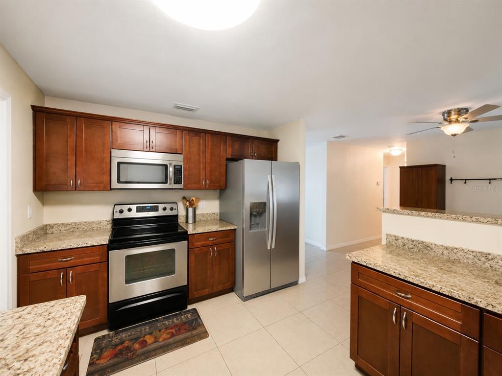 A kitchen features wood cabinets, granite countertops, stainless steel appliances, and tile flooring — 5814 HAMMON DRIVE, TAMPA, FL