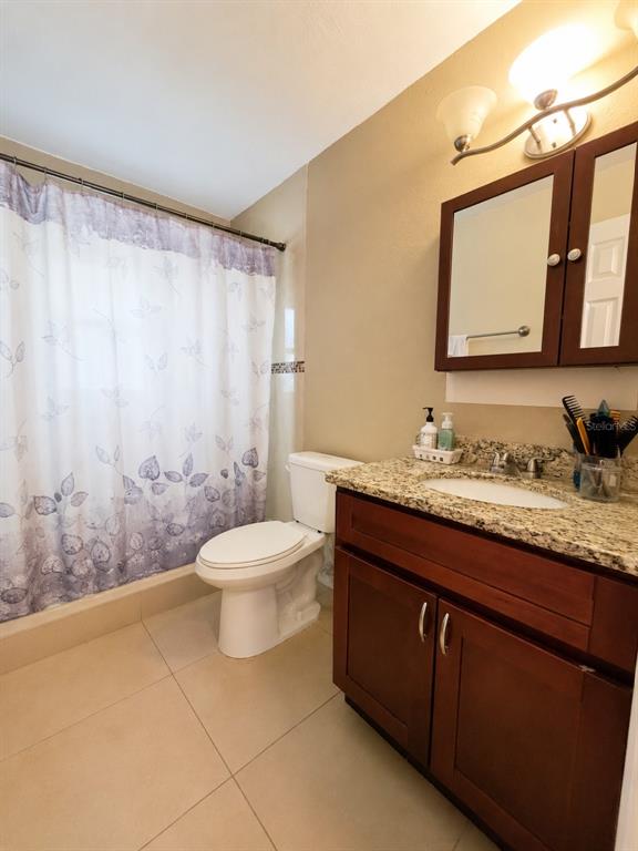 A bathroom features a wood vanity with a granite countertop, a toilet, and a shower curtain — 5814 HAMMON DRIVE, TAMPA, FL