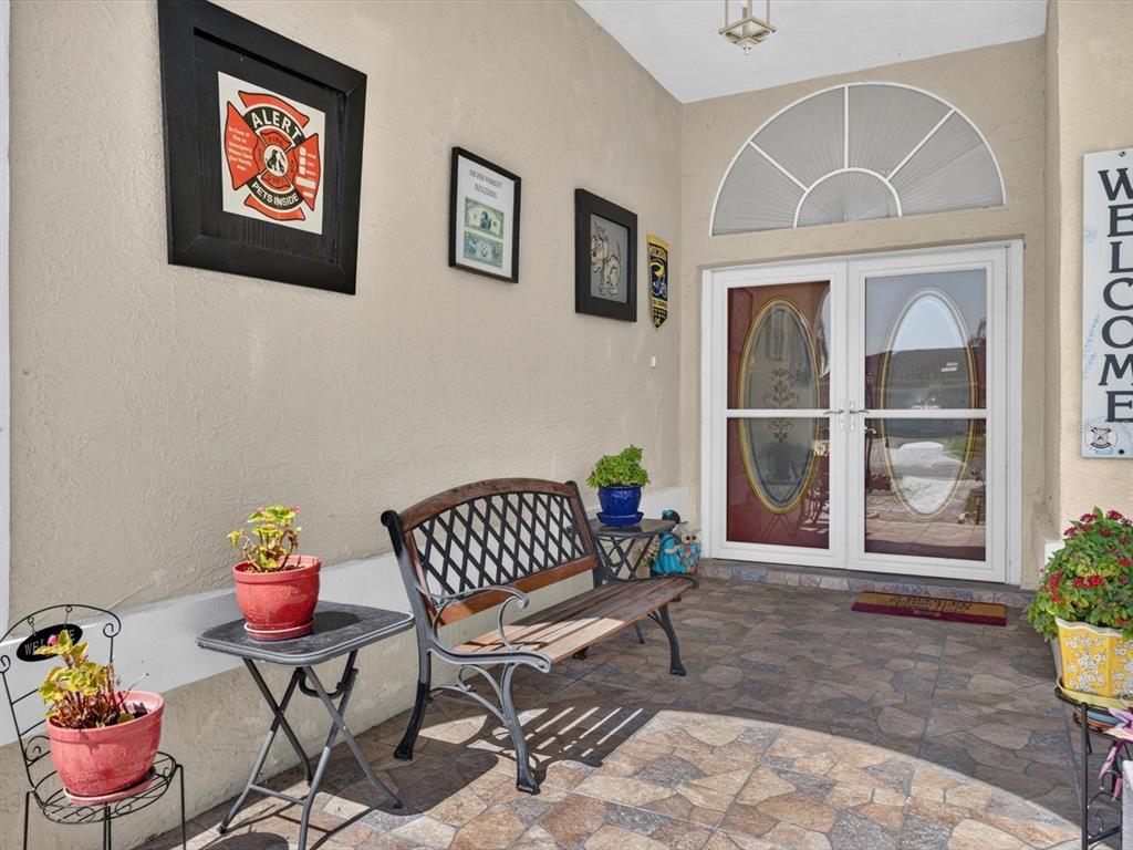 A covered porch features a bench, potted plants, wall art, and double glass entry doors — 1197 MUSCOVY DR, SPRING HILL, FL