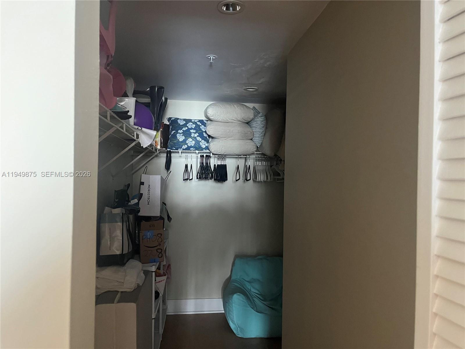 A walk-in closet features wire shelving, hanging clothes, stacked pillows, and a blue beanbag chair — 701 Brickell Key Blvd # 08, Miami FL 33131, MIAMI, FL