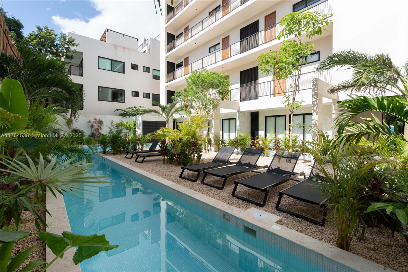 A narrow swimming pool sits beside a gravel patio with lounge chairs and apartment buildings — 1 Ave del Parque # 25, TX 77760, TX