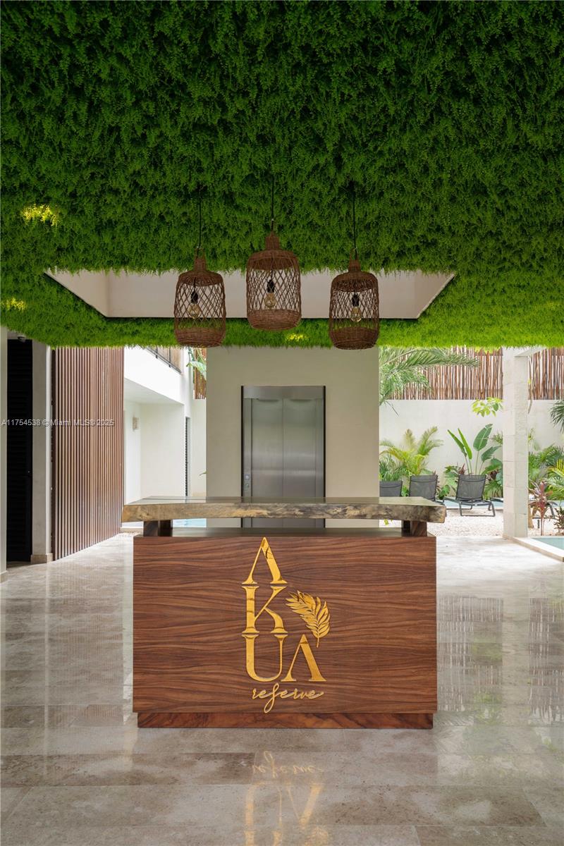 A wooden reception desk with a gold logo sits beneath a ceiling covered in greenery — 1 Ave del Parque # 25, TX 77760, TX