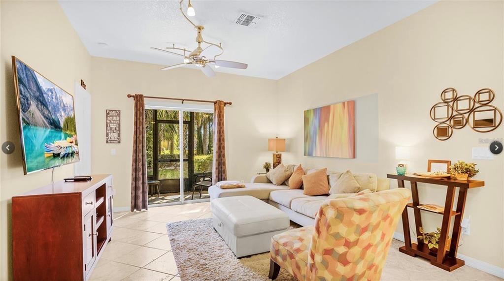 A living room with a sectional sofa, patterned armchair, television, and sliding glass patio doors — 2711 OAKWATER DRIVE UNIT 116, KISSIMMEE, FL