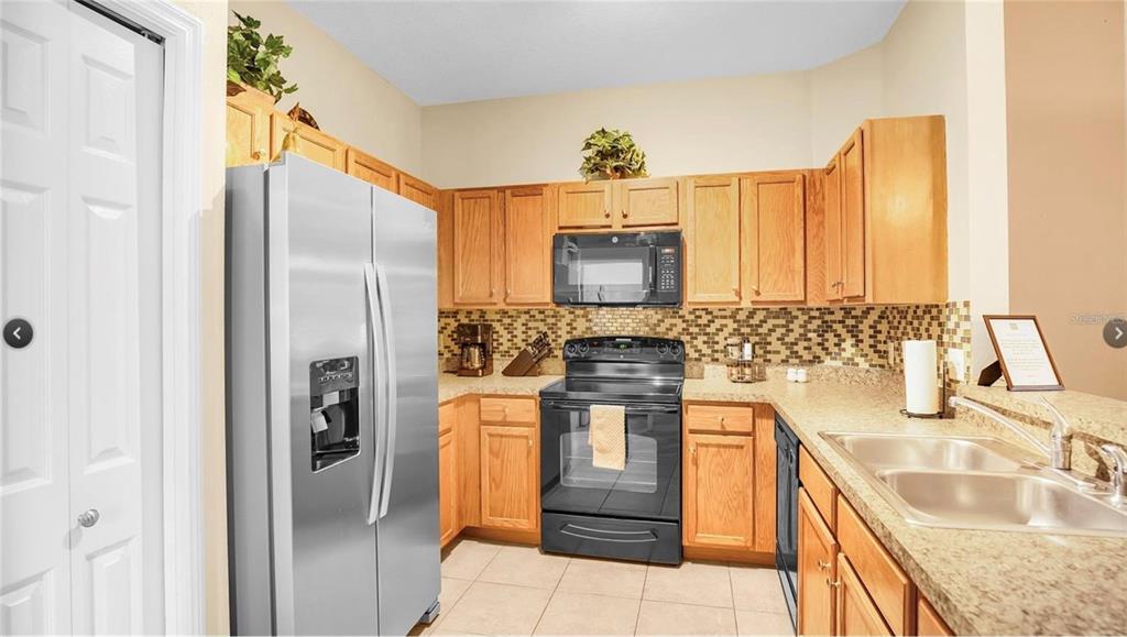 A kitchen features wood cabinets, stainless steel appliances, a tiled backsplash, and granite countertops — 2711 OAKWATER DRIVE UNIT 116, KISSIMMEE, FL