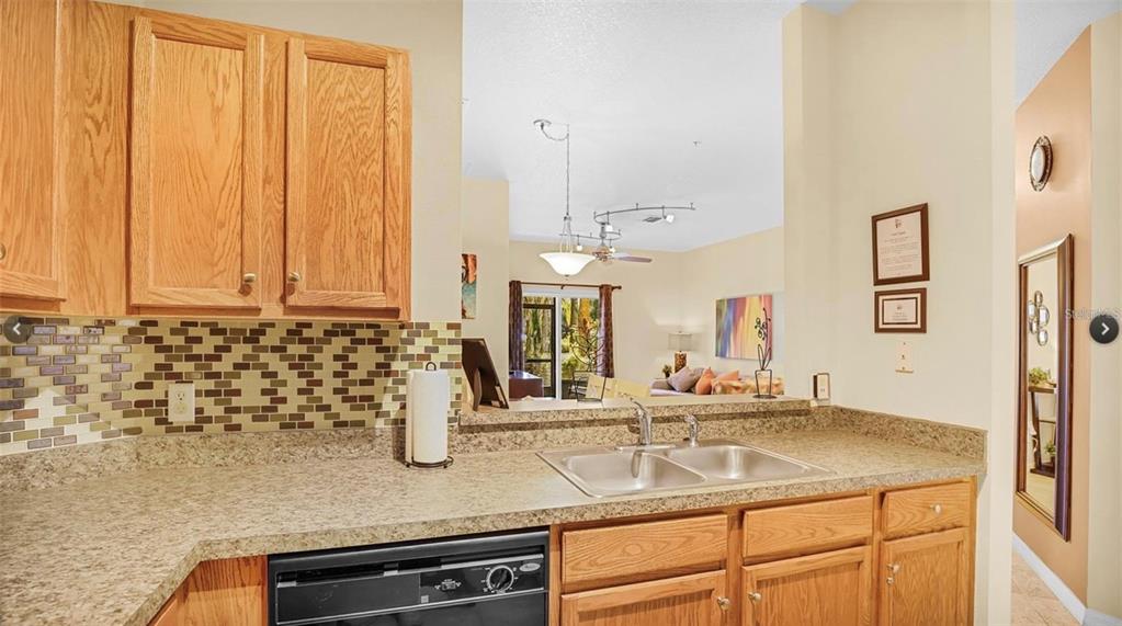 A kitchen features oak cabinets, a mosaic tile backsplash, and a double sink overlooking the living area — 2711 OAKWATER DRIVE UNIT 116, KISSIMMEE, FL