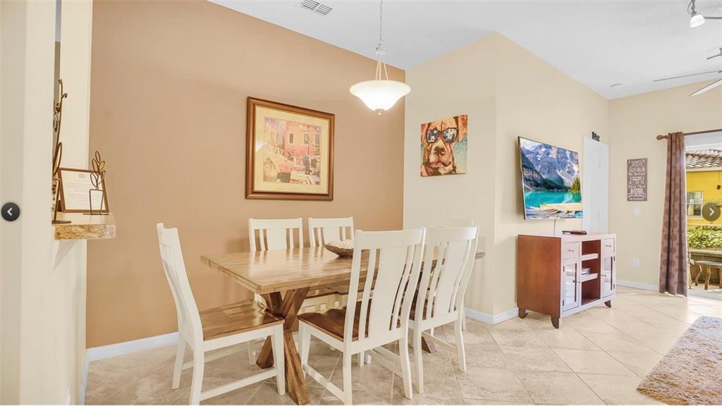 A dining area with a wooden table, white chairs, tile floors, and a wall-mounted television — 2711 OAKWATER DRIVE UNIT 116, KISSIMMEE, FL