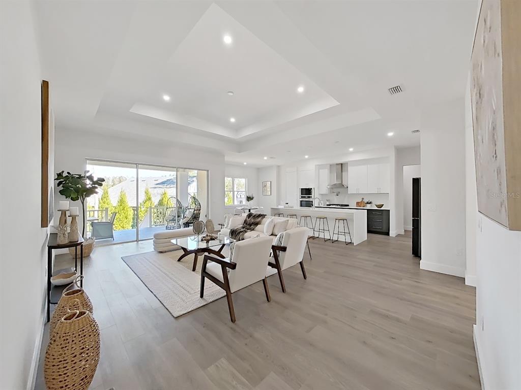 An open-concept living room and kitchen feature light wood flooring, a tray ceiling, and sliding doors — 4716 HICKORY OAK DRIVE, BROOKSVILLE, FL