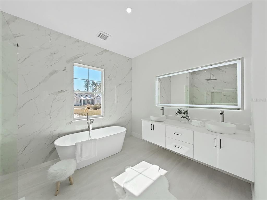 A modern bathroom features a white freestanding tub, double vanity, and marble-look wall tiles — 4716 HICKORY OAK DRIVE, BROOKSVILLE, FL