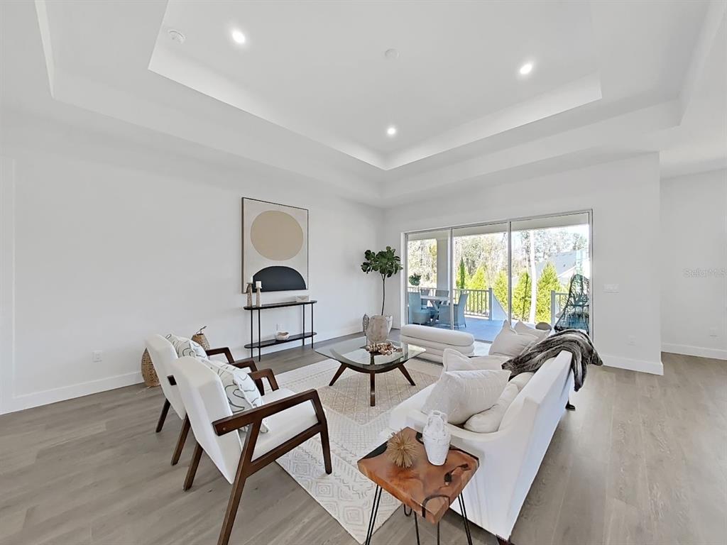 A bright living room features a tray ceiling, white furniture, and sliding glass doors — 4716 HICKORY OAK DRIVE, BROOKSVILLE, FL