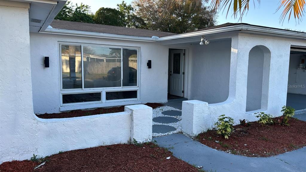 A white stucco house exterior features a covered entryway, a large window, and a walkway — 1715 KENILWORTH STREET, HOLIDAY, FL