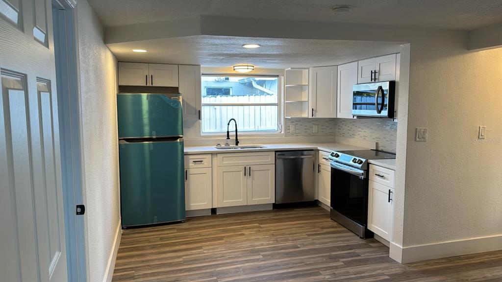A kitchen features white cabinets, stainless steel appliances, a window, and wood-look flooring — 1715 KENILWORTH STREET, HOLIDAY, FL