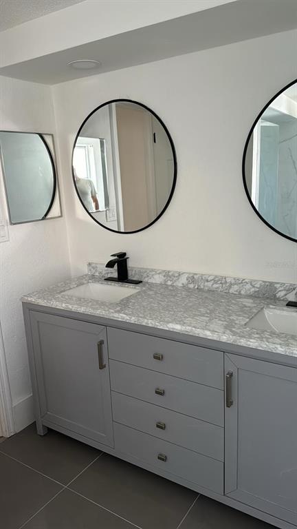 A bathroom vanity with a marble countertop, two sinks, and gray cabinets under round mirrors — 1715 KENILWORTH STREET, HOLIDAY, FL