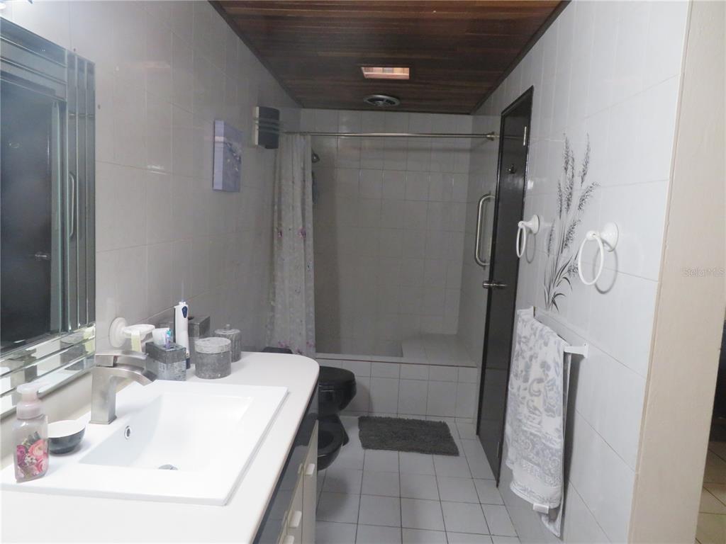 A bathroom features a white vanity, a tiled shower with a bench, and wood-paneled ceiling — Dorado del Mar PELICANO, DORADO, PR