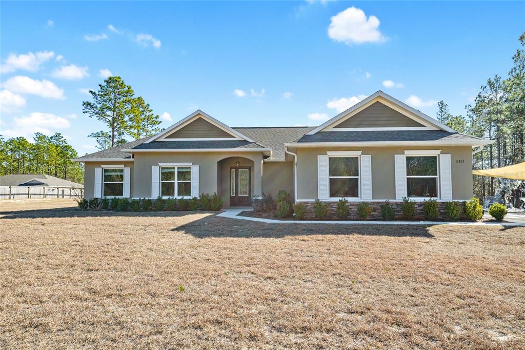 A single-story house with a tan stucco exterior, stone accents, and a gabled roof — 8855 SW 129TH TERRACE ROAD, DUNNELLON, FL