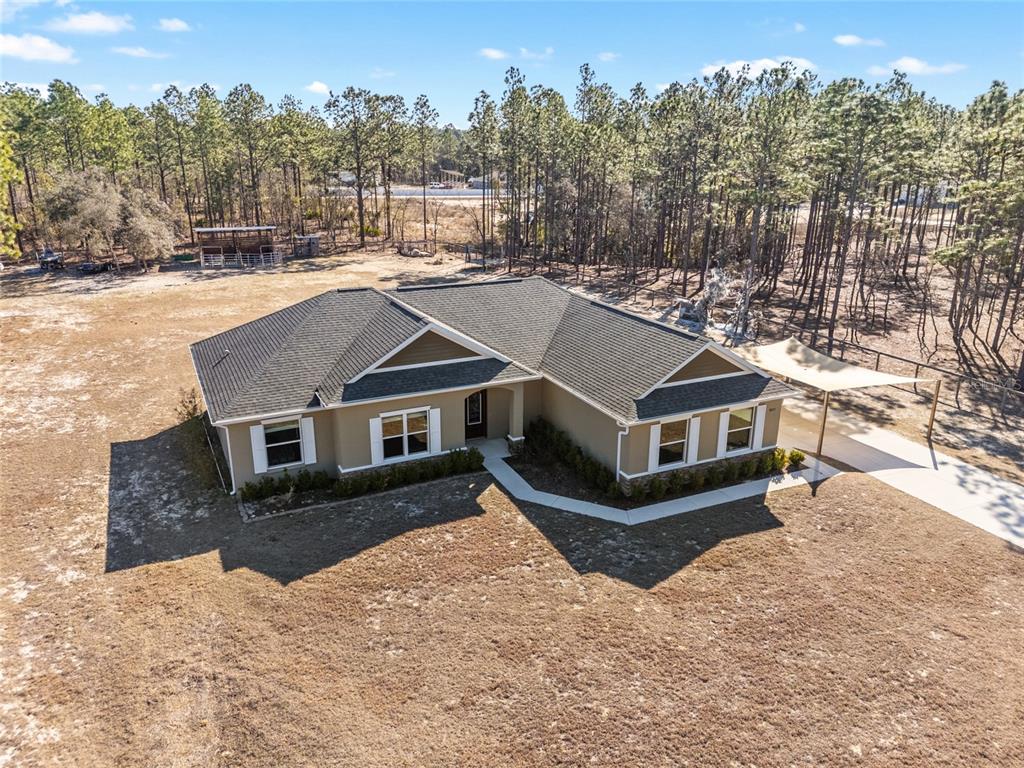An aerial view shows a tan, single-story house with a dark shingled roof and driveway — 8855 SW 129TH TERRACE ROAD, DUNNELLON, FL