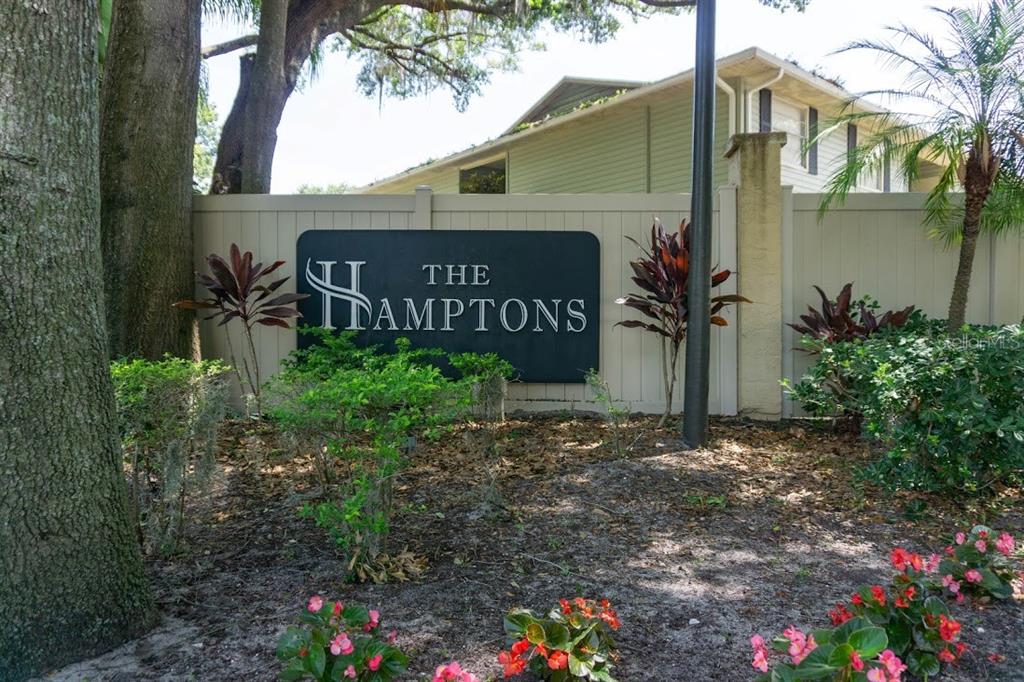 A sign for The Hamptons stands in front of a beige fence and landscaping — 510 GOLDEN RAINTREE PLACE, BRANDON, FL