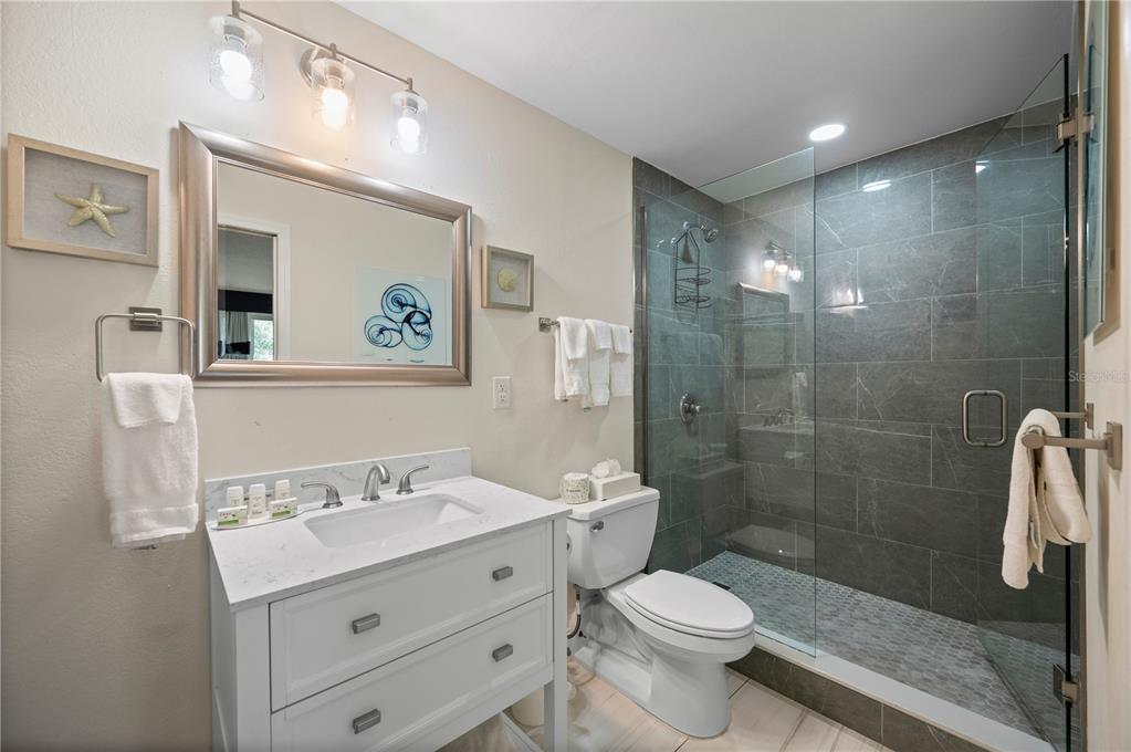 A bathroom features a white vanity, a toilet, and a glass-enclosed shower with gray tiles — 7150 N TAMIAMI TRAIL UNIT S-600, SARASOTA, FL