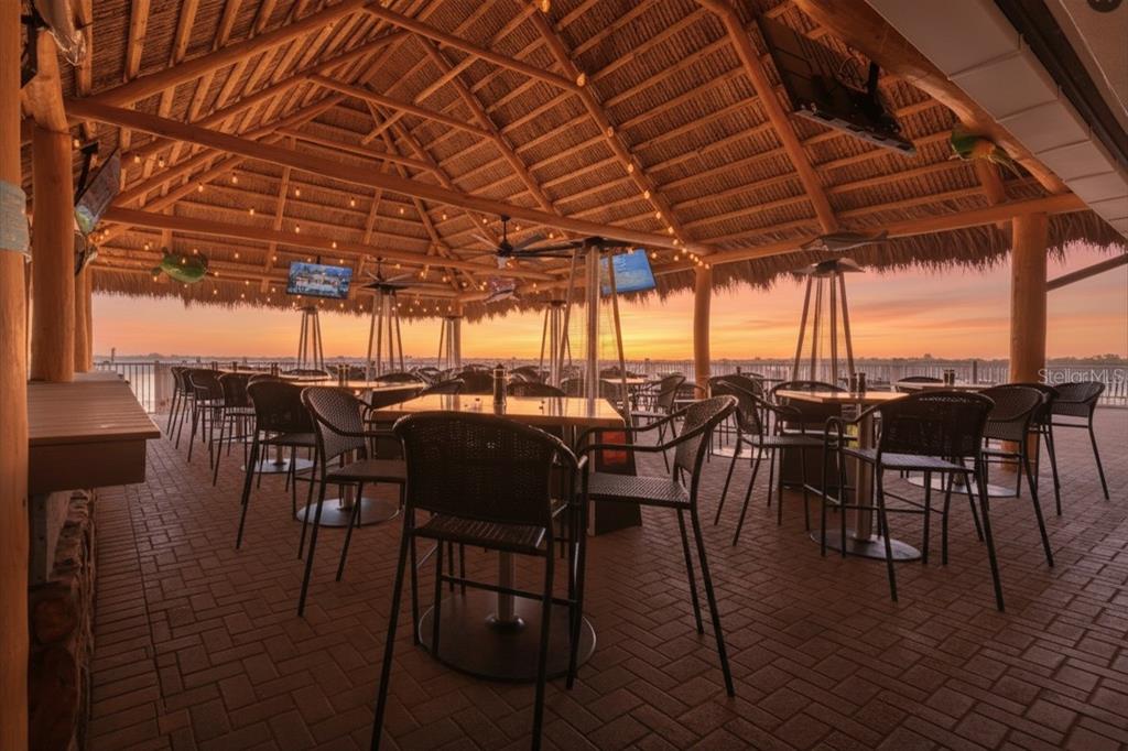 An outdoor covered patio with a thatched roof, brick flooring, and tables overlooking a sunset — 7150 N TAMIAMI TRAIL UNIT S-600, SARASOTA, FL