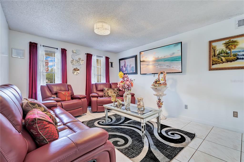A living room features burgundy leather furniture, a glass coffee table, and a wall-mounted television — 9824 SURREY RIDGE ROAD, ORLANDO, FL
