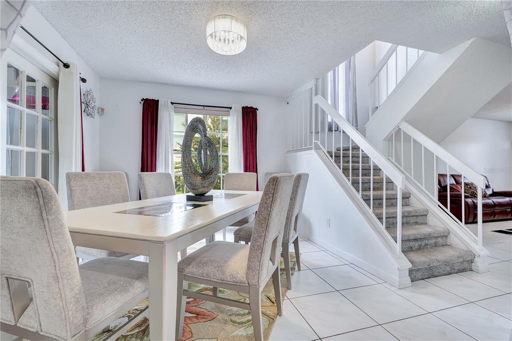 A dining room with a light-colored table, upholstered chairs, tile flooring, and a carpeted staircase — 9824 SURREY RIDGE ROAD, ORLANDO, FL