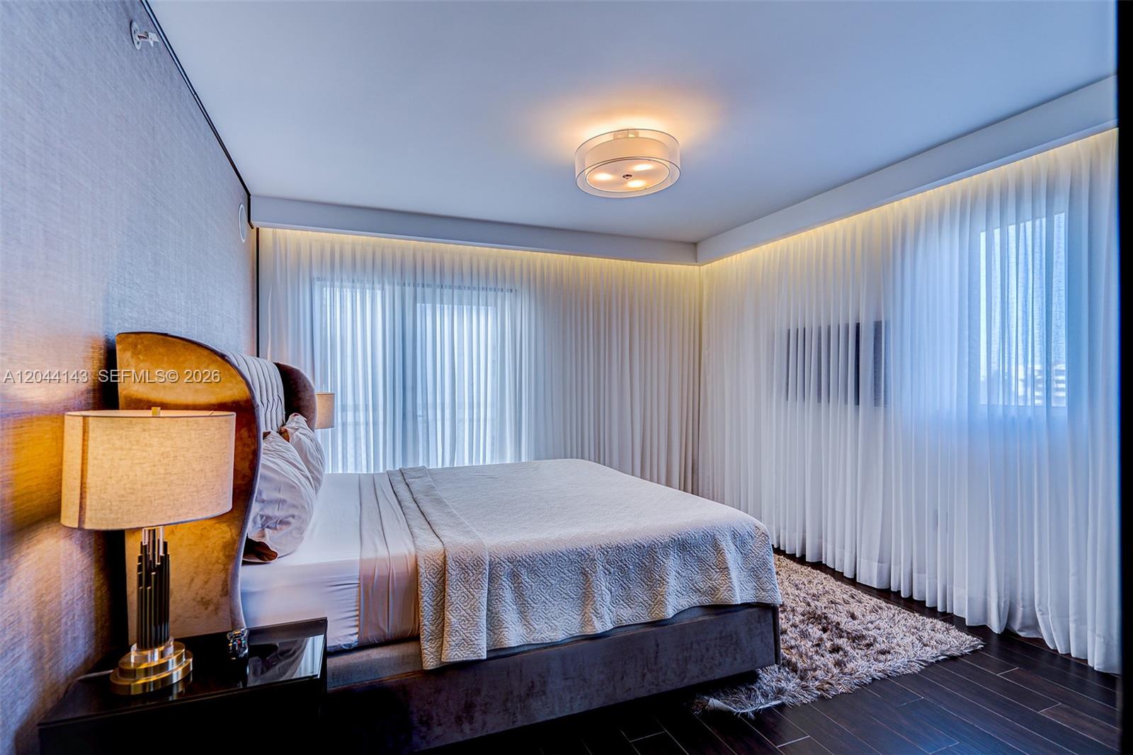 A bedroom features a bed with a tufted headboard, floor-to-ceiling curtains, and dark wood flooring — 1701 Sunset Harbour Dr # L507, Miami Beach FL 33139, MIAMI BEACH, FL