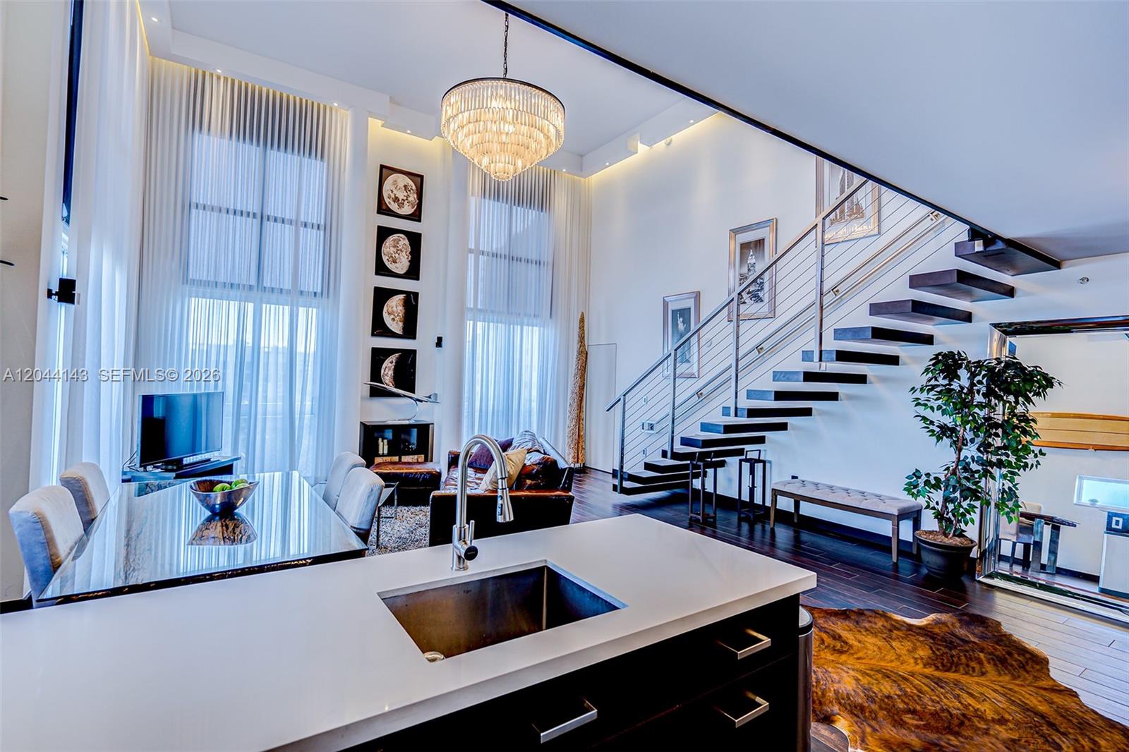 A modern, high-ceilinged living and dining area features a floating staircase and kitchen island — 1701 Sunset Harbour Dr # L507, Miami Beach FL 33139, MIAMI BEACH, FL