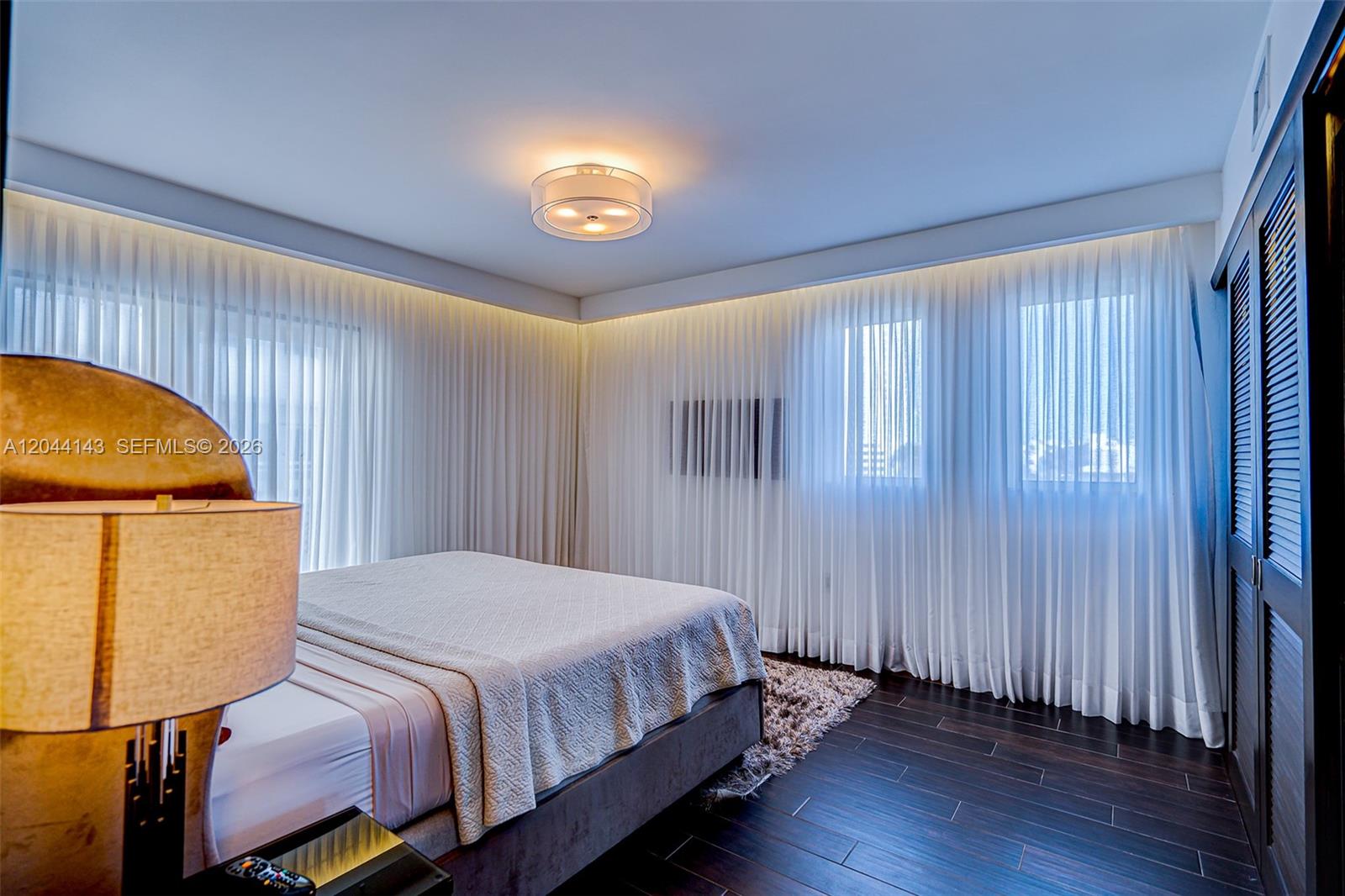 A bedroom features dark wood flooring, a bed with a textured cover, and floor-to-ceiling curtains — 1701 Sunset Harbour Dr # L507, Miami Beach FL 33139, MIAMI BEACH, FL