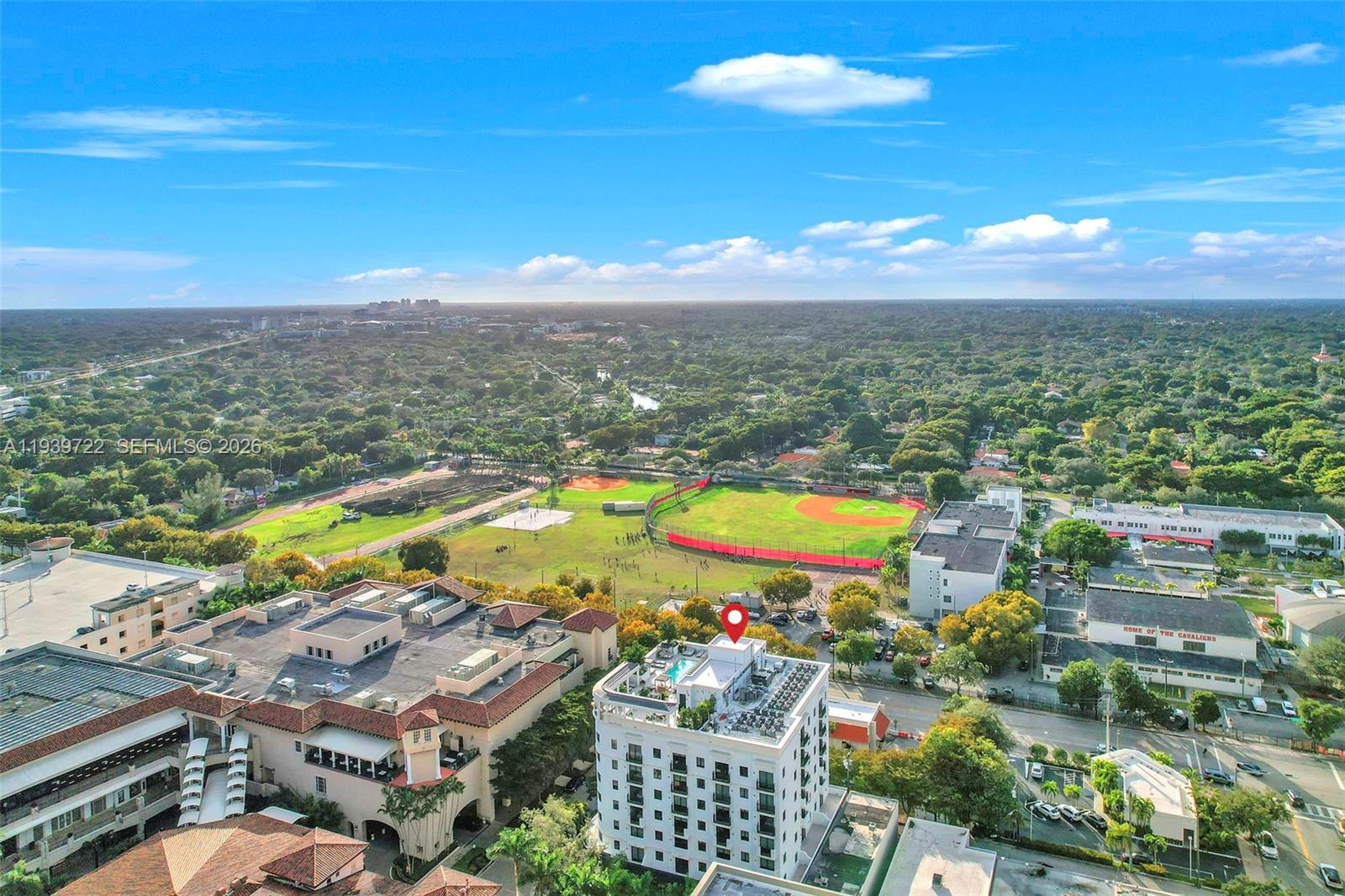 An aerial view shows a multi-story building with a rooftop pool near a baseball field — 4220 Laguna St # 505, Coral Gables FL 33146, CORAL GABLES, FL