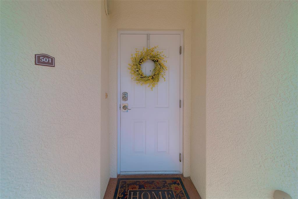A white front door with a yellow wreath and a welcome mat at the entrance — 17735 GULF BOULEVARD UNIT 501, REDINGTON SHORES, FL