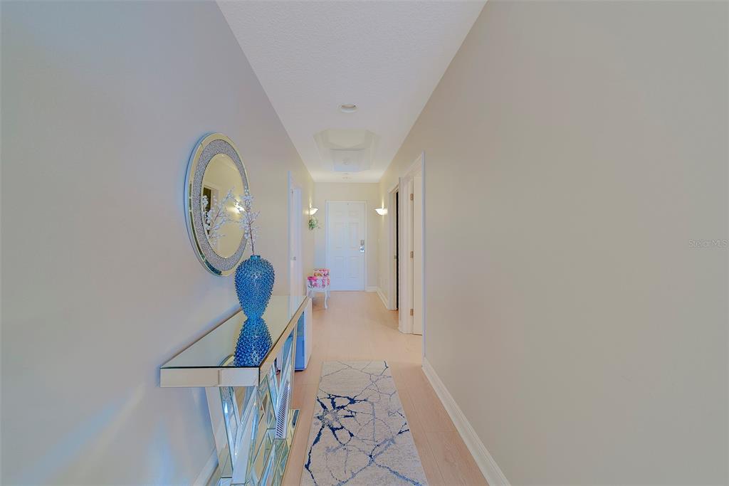 A hallway features light wood flooring, a mirrored console table, and a circular wall mirror — 17735 GULF BOULEVARD UNIT 501, REDINGTON SHORES, FL