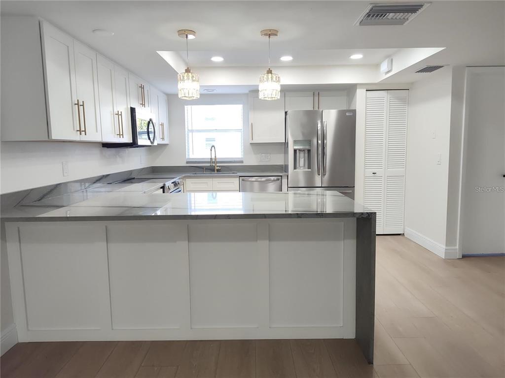 A modern kitchen features white cabinetry, stainless steel appliances, and a large gray-veined island — 255 CAPRI CIRCLE N UNIT 36, TREASURE ISLAND, FL