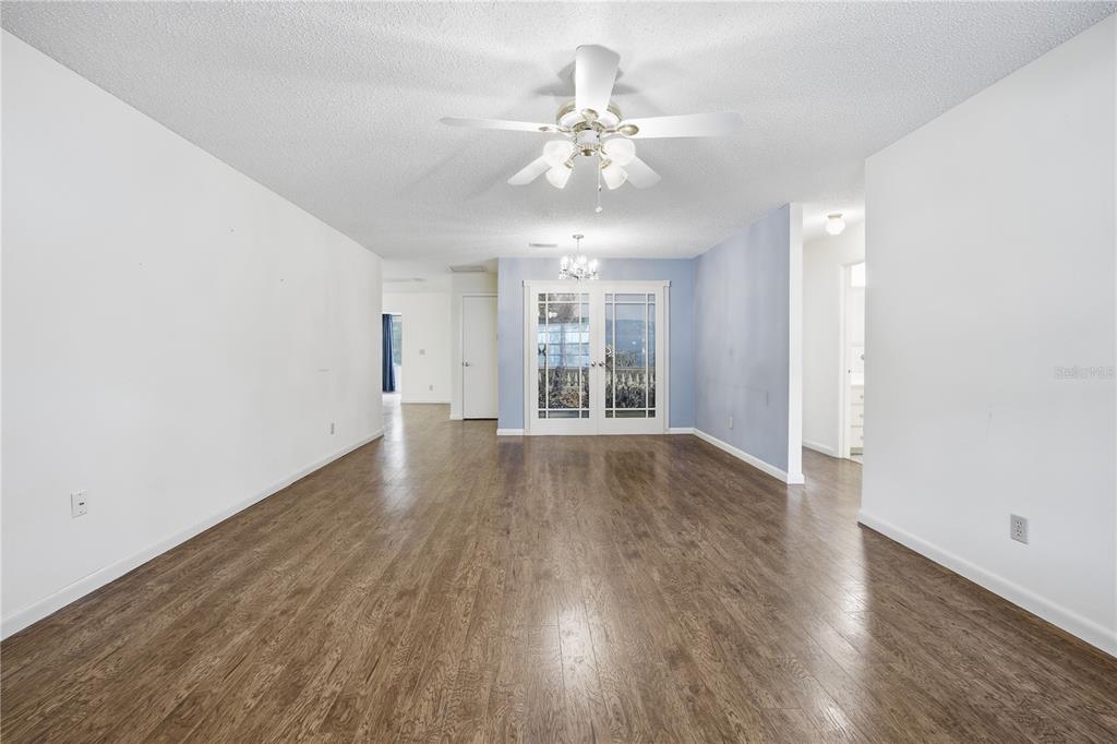 A spacious room with wood-look flooring, white walls, a ceiling fan, and French doors — 8666 SW 92ND LANE UNIT F, OCALA, FL