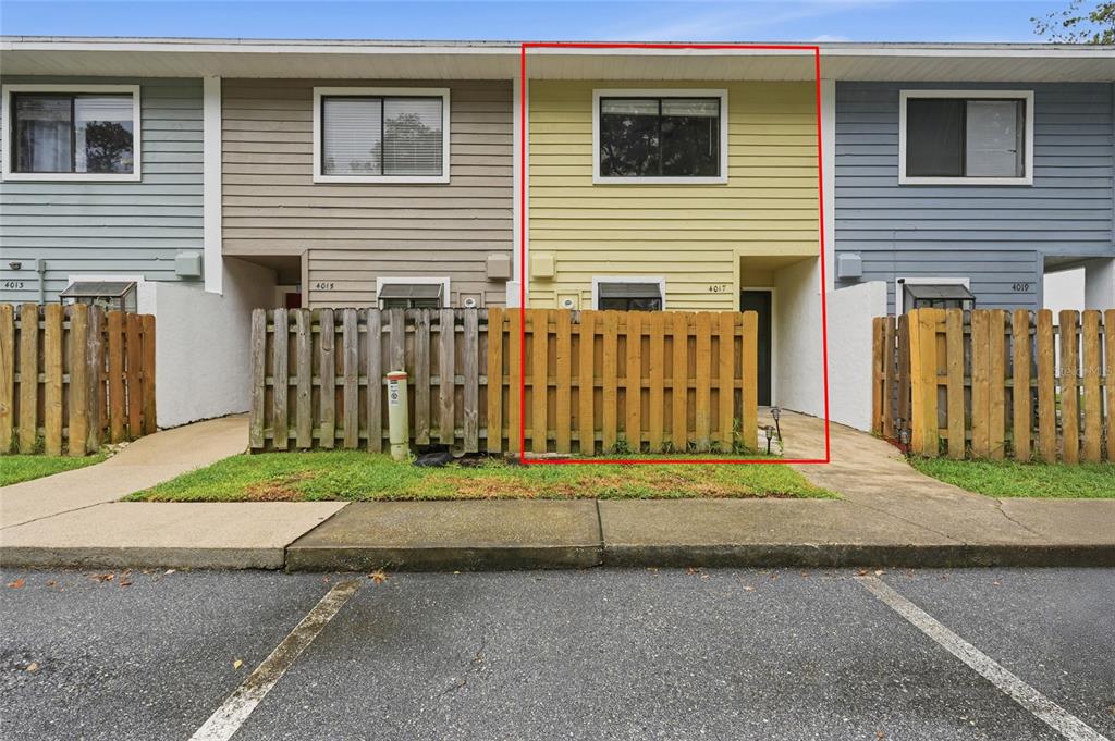 A yellow two-story townhouse unit features a wooden privacy fence and a concrete walkway — 4017 SW 20TH LANE, GAINESVILLE, FL
