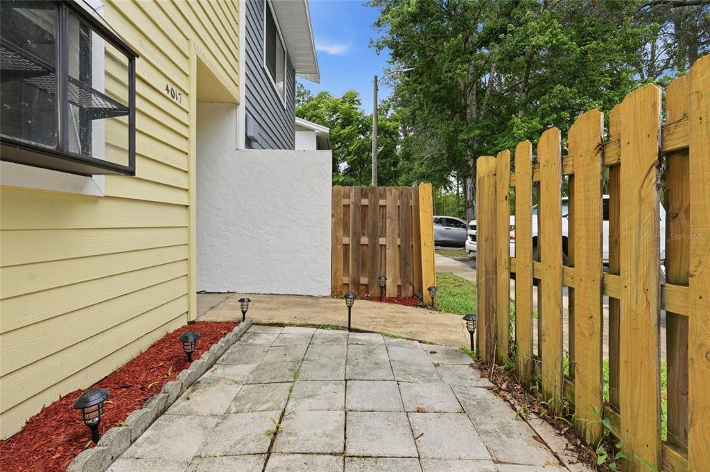 A paved walkway leads to the entrance of a yellow house with a wooden fence — 4017 SW 20TH LANE, GAINESVILLE, FL