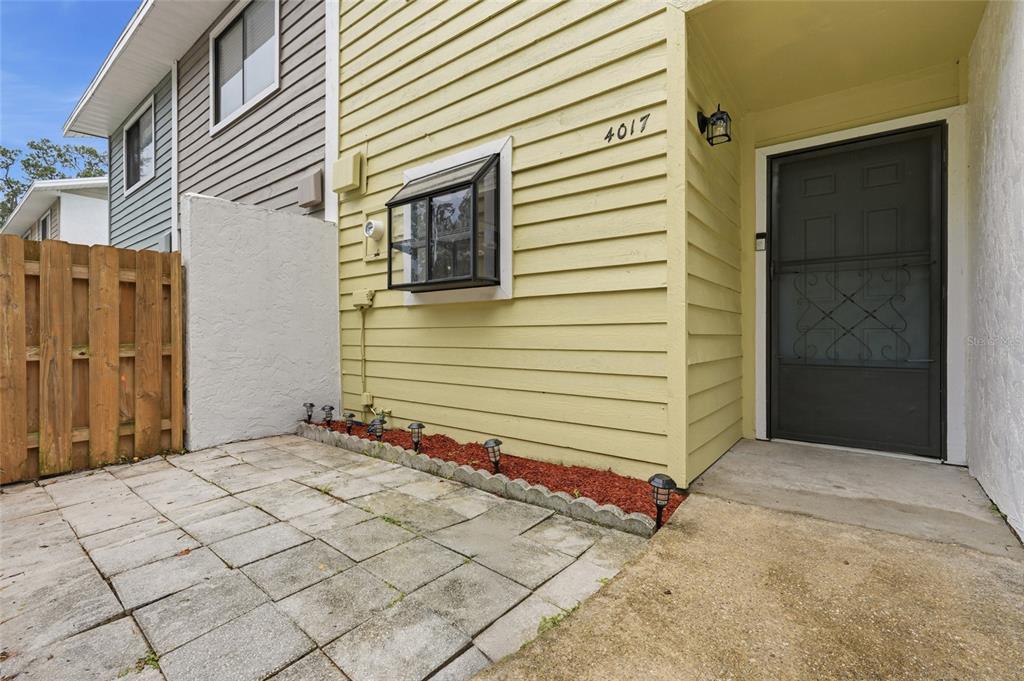 A paved patio sits in front of a yellow-sided house with a screen door — 4017 SW 20TH LANE, GAINESVILLE, FL