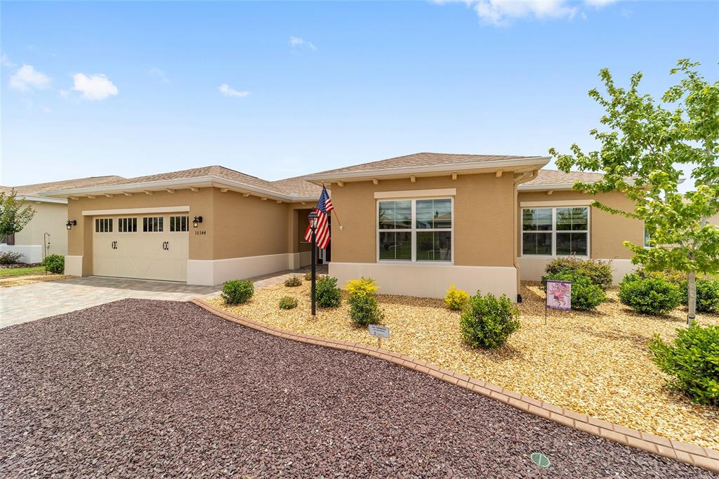 A single-story tan house with a two-car garage and a gravel front yard — 10344 SW 98TH PLACE ROAD, OCALA, FL