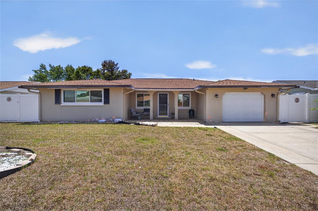 A single-story house with a tan stucco exterior, a brown shingled roof, and a garage — 10237 OAK HILL DRIVE, PORT RICHEY, FL
