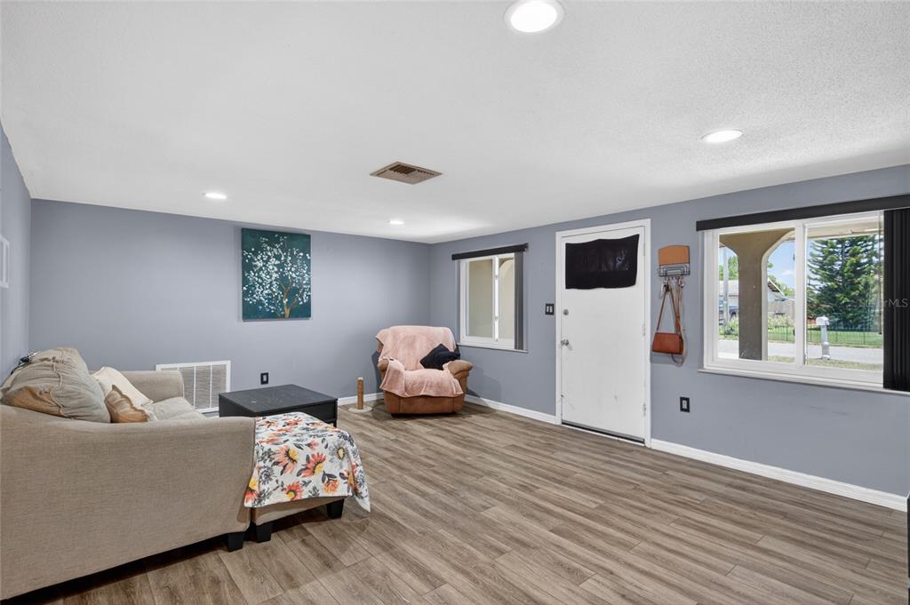 A living room with gray walls, wood-look flooring, a sofa, a recliner, and a front door — 10237 OAK HILL DRIVE, PORT RICHEY, FL