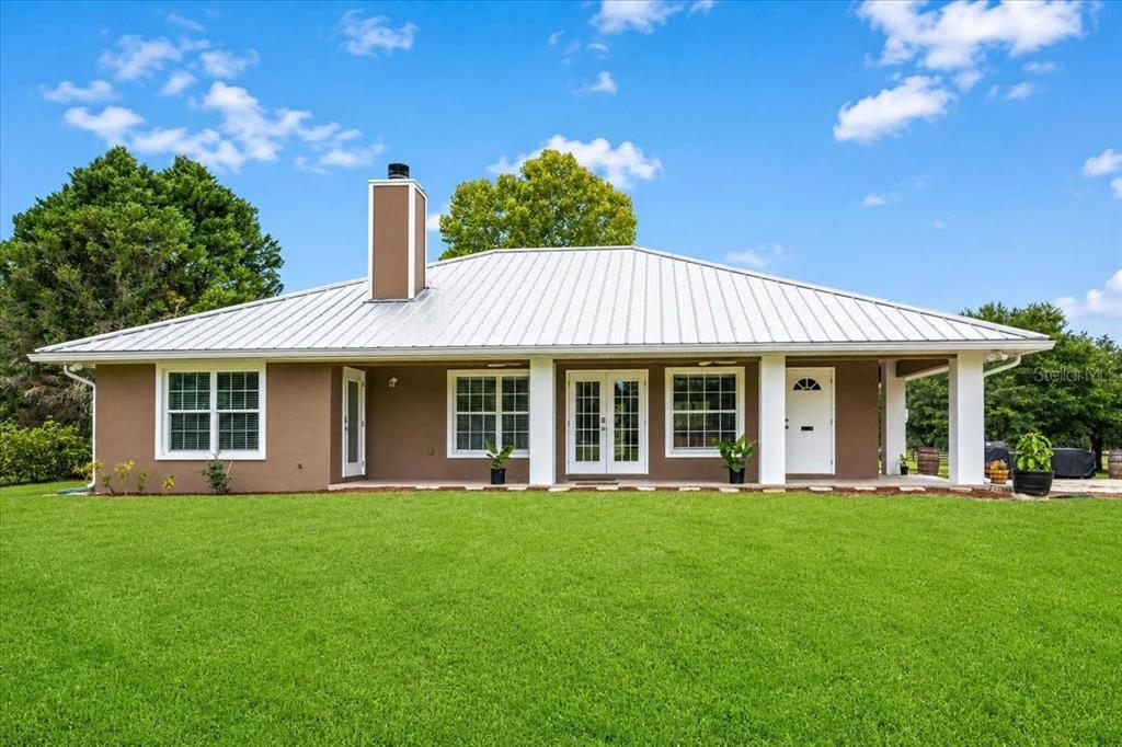 The exterior of a one-story house with a metal roof, brown stucco walls, and lawn — 14681 NW 232ND STREET, HIGH SPRINGS, FL