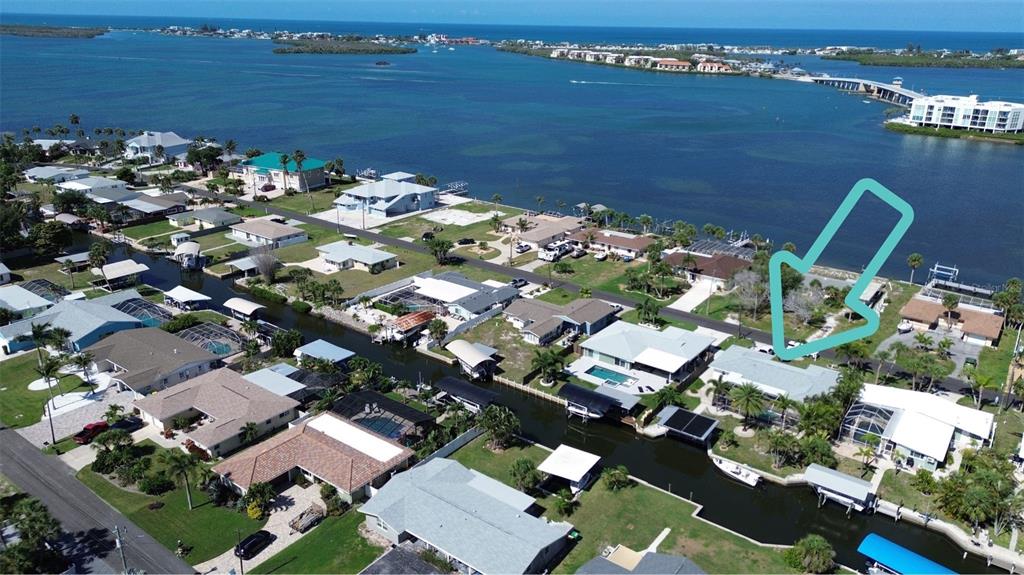 An aerial view shows waterfront homes along a canal with a turquoise arrow pointing toward a lot — 1433 LEMON BAY DRIVE, ENGLEWOOD, FL